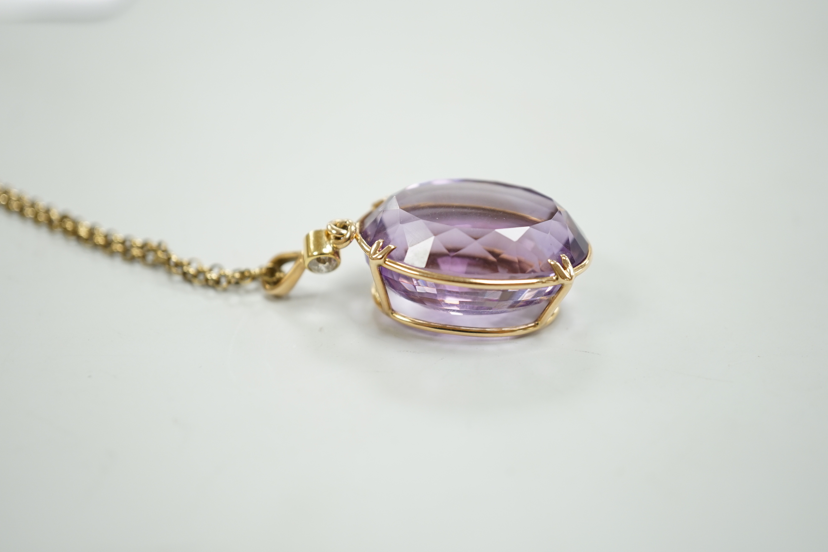 An early 20th century 15ct and single stone oval cut amethyst set pendant, with single stone diamond set bale, overall 42mm, on a gold plated chain.